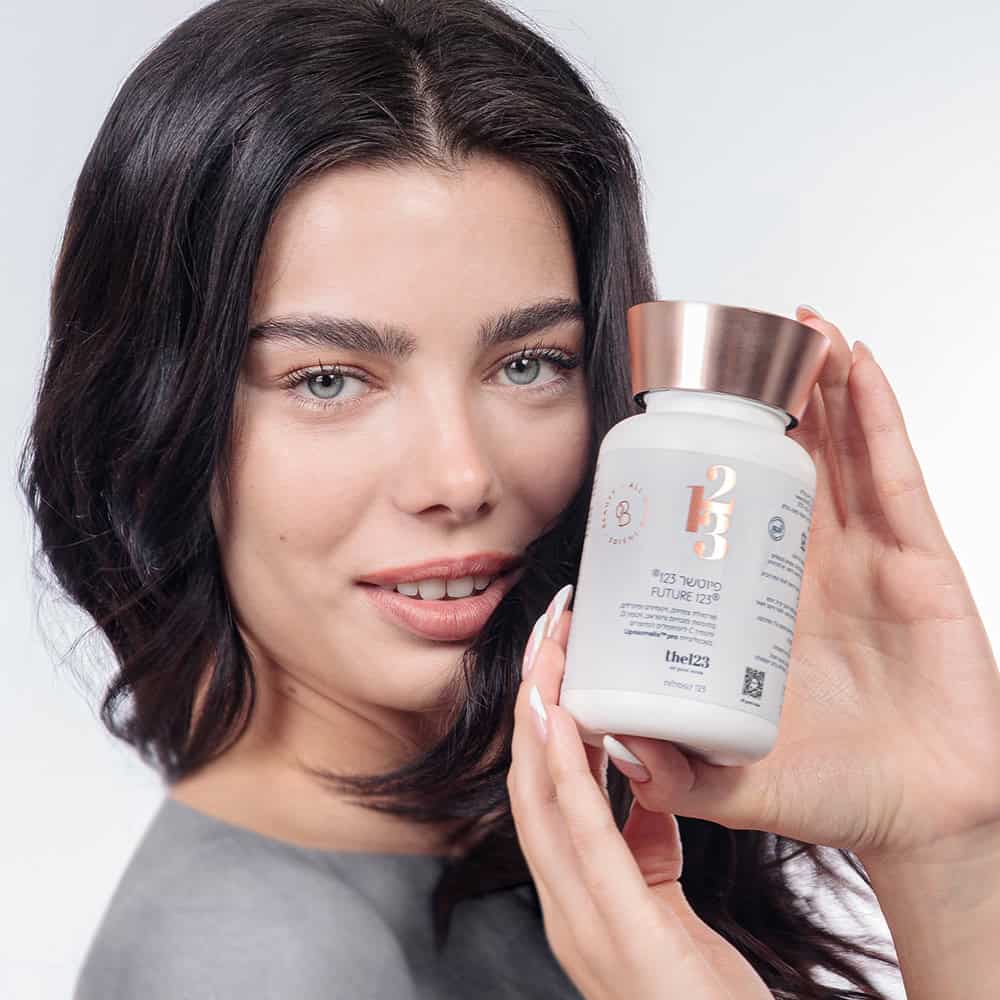 אישה צעירה נאה בעלת שיער בריא ושופע מחזיקה בידיה מוצר תזונה פיוטשר 123 קפסולות