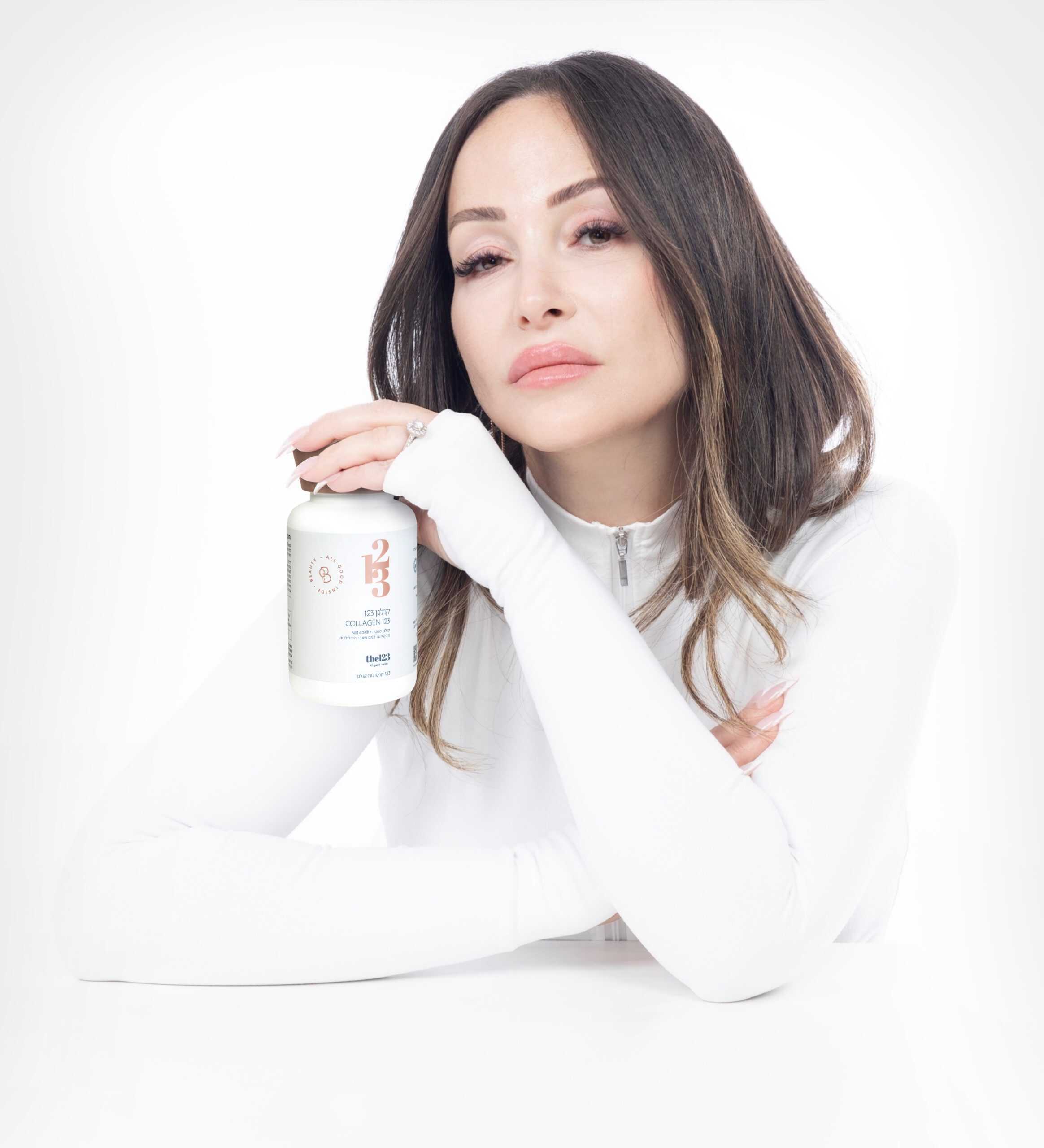 אישה נאה מסתכלת למצלמה, כאשר היא מחזיקה בידה קולגן 123